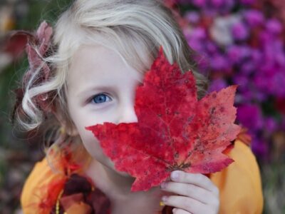 Young girl holding autumn leaf against her face